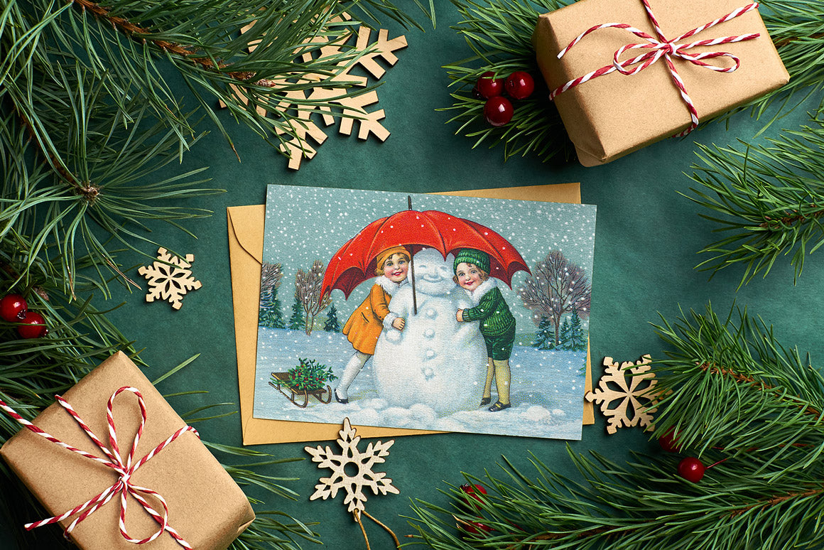 Lovely card flatlay of a greeting card with children and a snowman using the Vintage Christmas Illustrations Compendium extended license graphics collection.